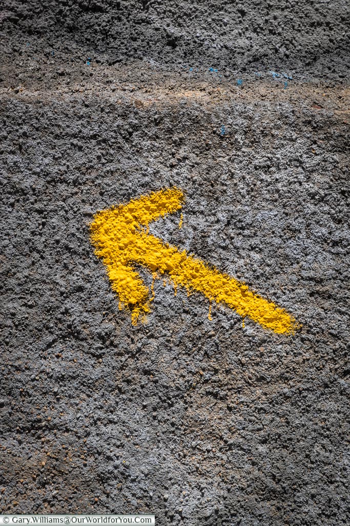 A yellow painted arrow on grey stonework in León, Spain.