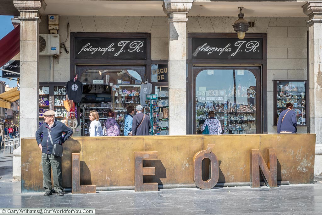 An elderly gentleman is standing next to the waist-high bronze town sign for León in Northern Spain.