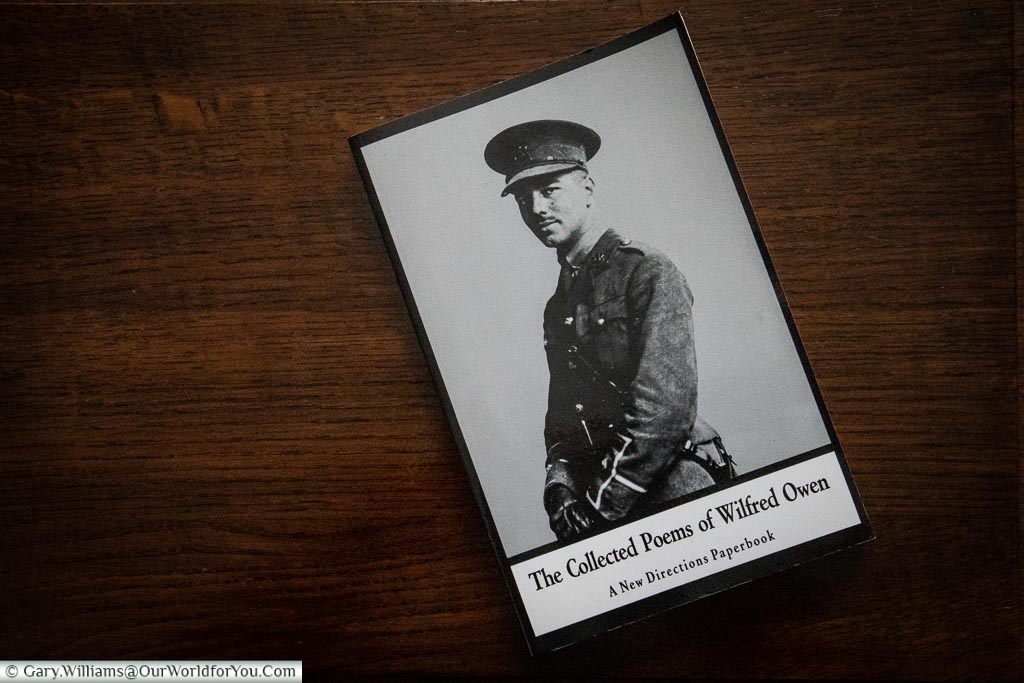 A copy of the book, 'The Collected Poems of Wilfred Owen', featuring an image of the soldier, placed on a side table.