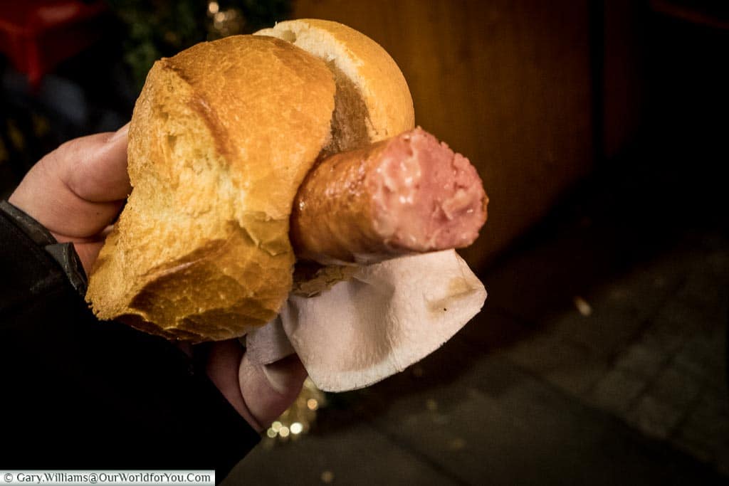 Gary holding a bread roll containing a German cheese sausage.  The cheese sausage is the normal pork variety blended with cheese, so it oozes from the sausage.
