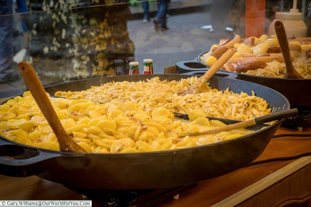 A large cast-iron open dish of Knepfle or Spaetzle, alongside another dish of Choucroute Garnie, on a Christmas market stall.