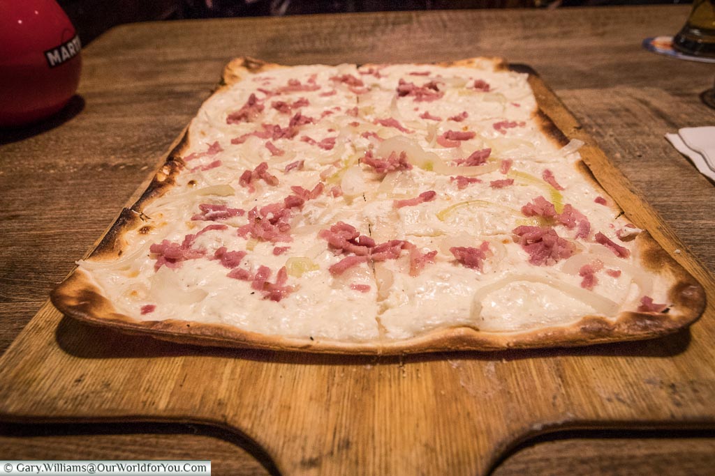 A thin and crispy Tarte flambée, A speciality of the Alsace region, topped with crème fraiche, thinly sliced onions and fine lardons of smoked bacon