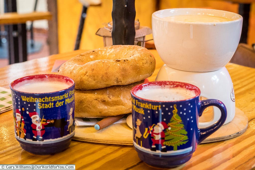 Two mugs of gluhwein in front of a fondue served with two rustic bread rolls served up on a Christmas market stall in Römerberg.