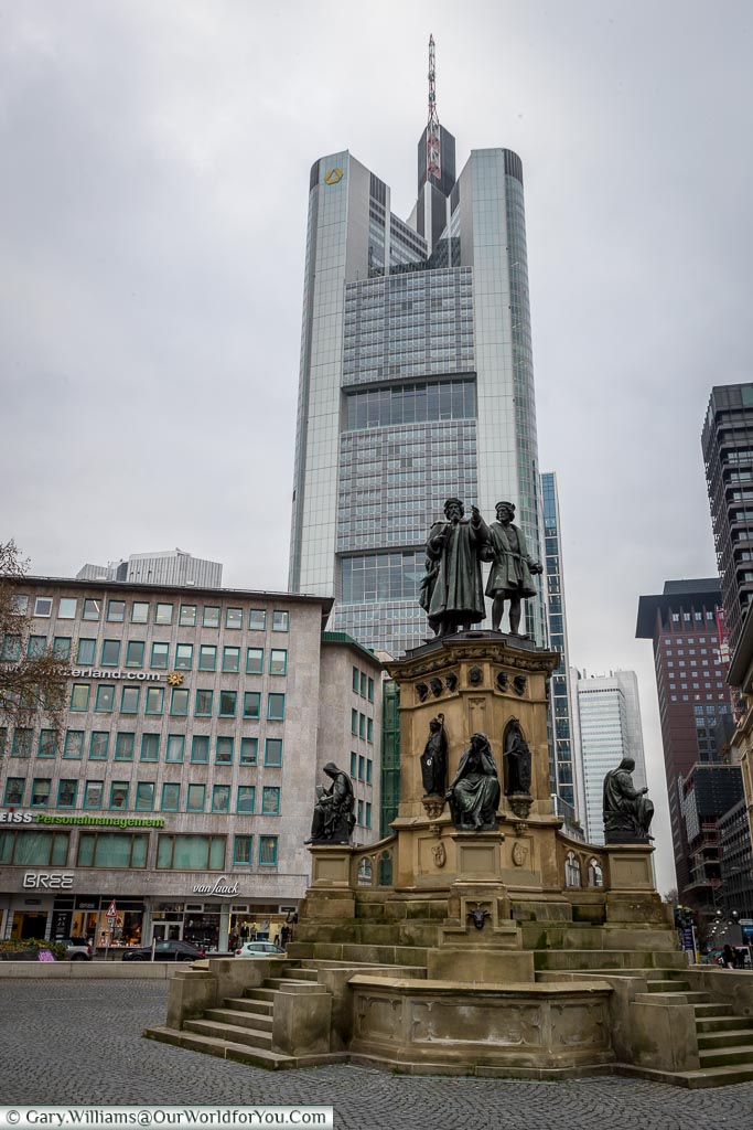 The Gutenberg Memorial in Frankfurt in front of a skyscraper.  The memorial is to Johannes Gutenberg, credited as the inventor of the modern printing press.