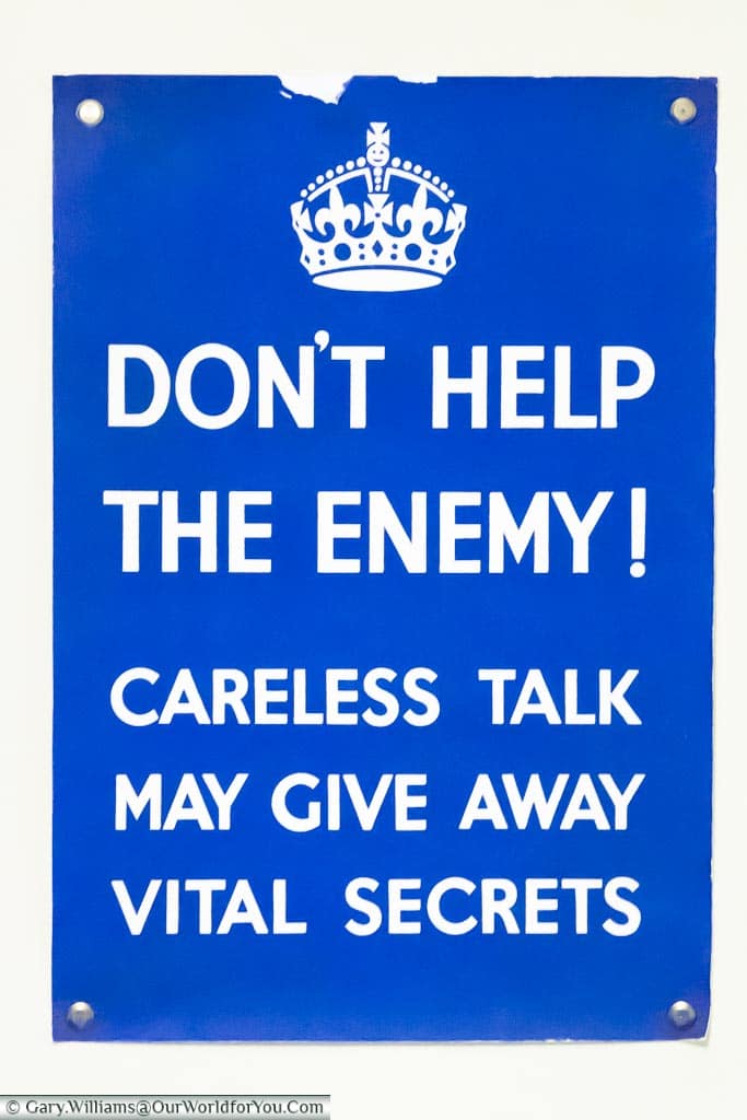 An official government blue sign with white writing stating 'Don't help the enemy'; careless talk may give away vital secrets.