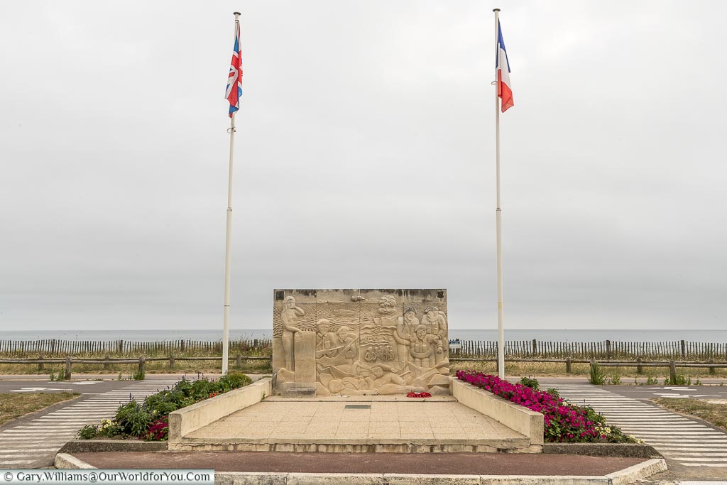 A memorial on Sword beach in Normandy.  The stone monument flanked by two flag poles, the Union flag atop one, the French Tricolour the other.