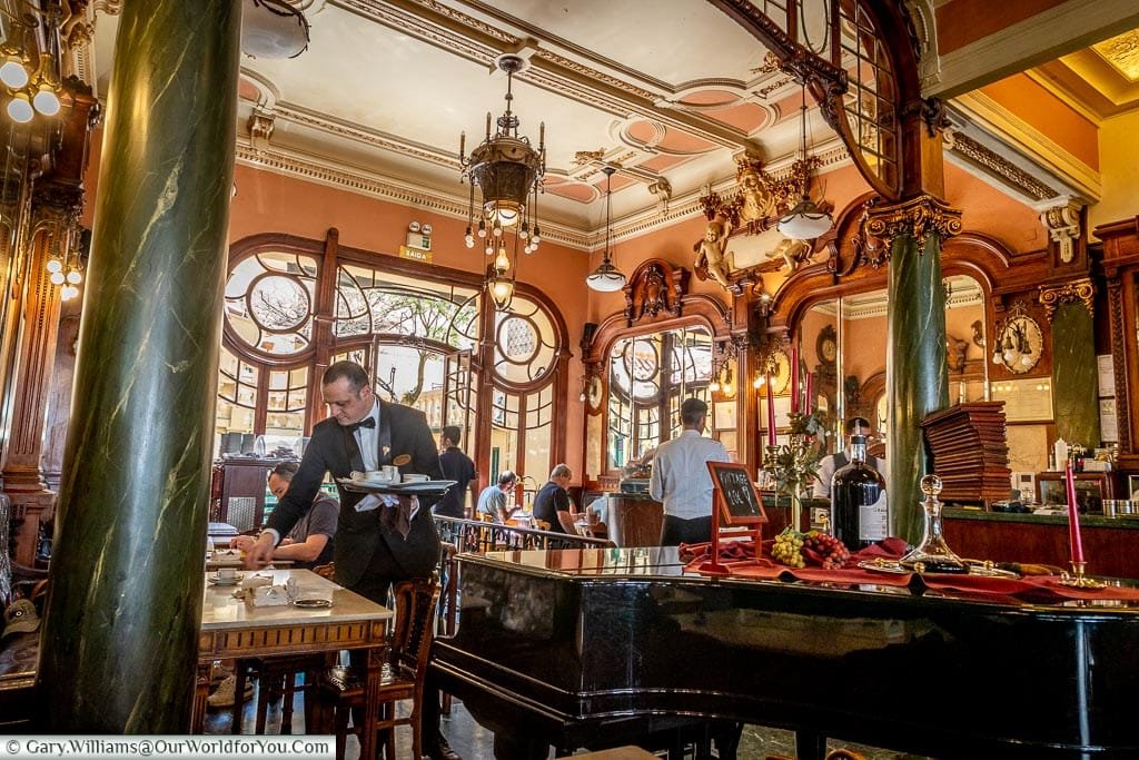 A large polished grand piano between two marble pillars in the beautifully ornate interior of the Majestic café, Porto, Portugal