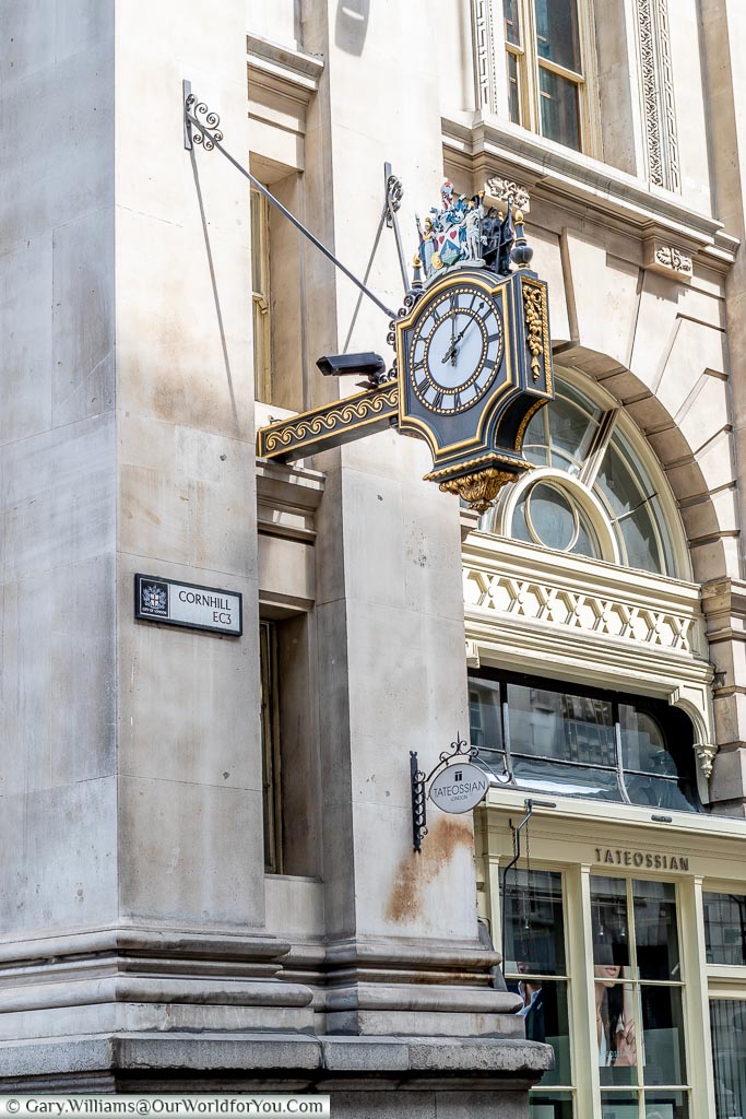 An ornate street clock suspended above a sign for Cornhill in the EC3 area of the City of London
