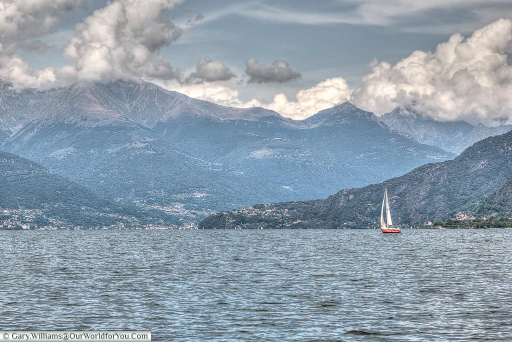 A small sail boat on the Lake Como dwarfed by the mountains the surround the north of the lake.