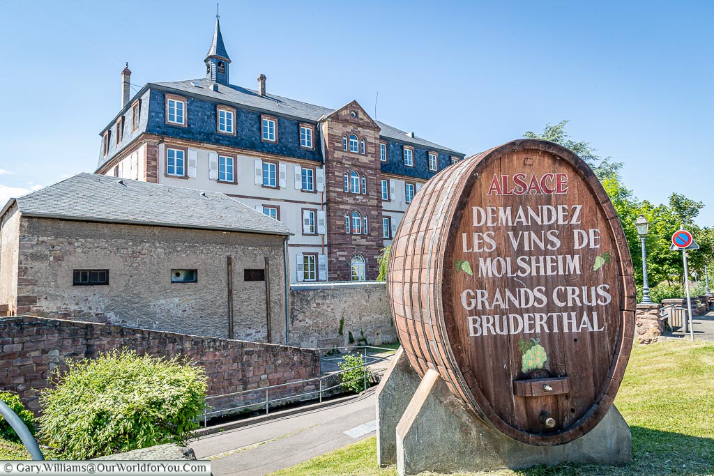 A large oak wine barrel in front of a grand building. The writing on the oak barrel states 'demand the wines of Molsheim' - in French of course.