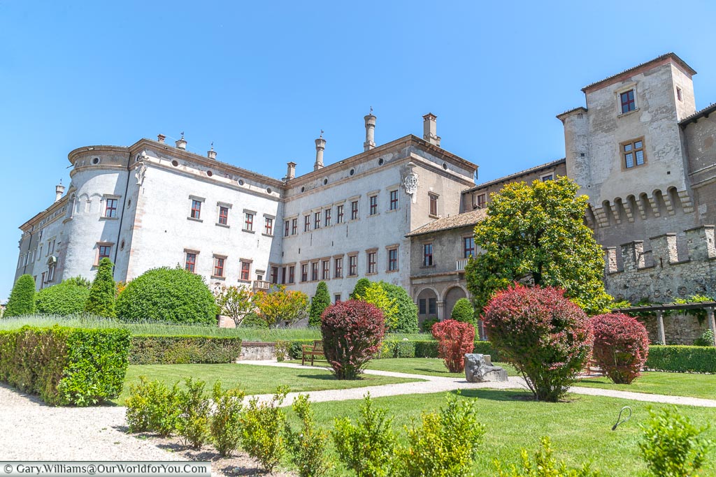 The gardens of the Buonconsiglio Castle Museum looking back of the white stone castle on a bright sunny day with clear blue skies.
