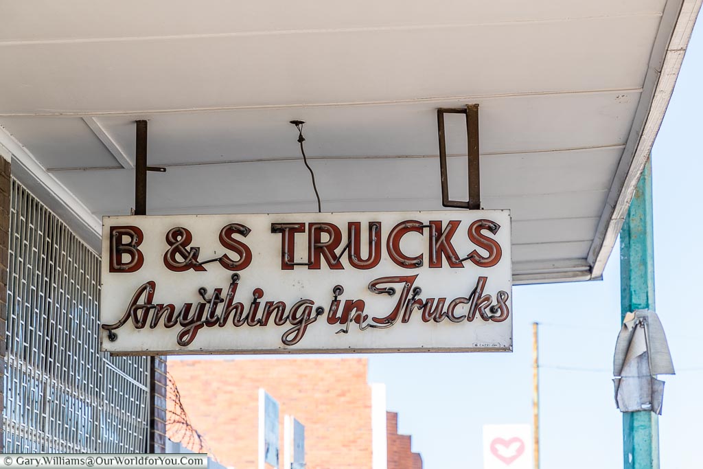 An old neon sign above the pavement that reads B&S Trucks - Anything in Truck