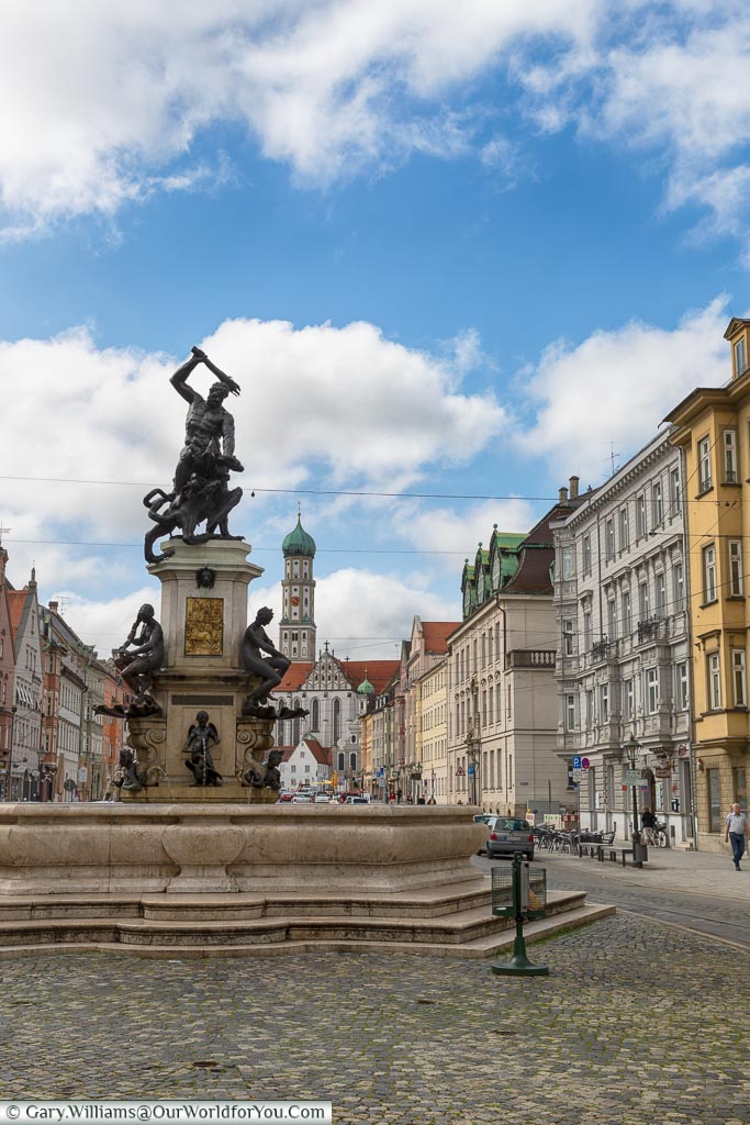 A street view of the Hercules fountain in Maximilianstraße with St. Ulrich’s and St Afra’s Abbey in the distance.