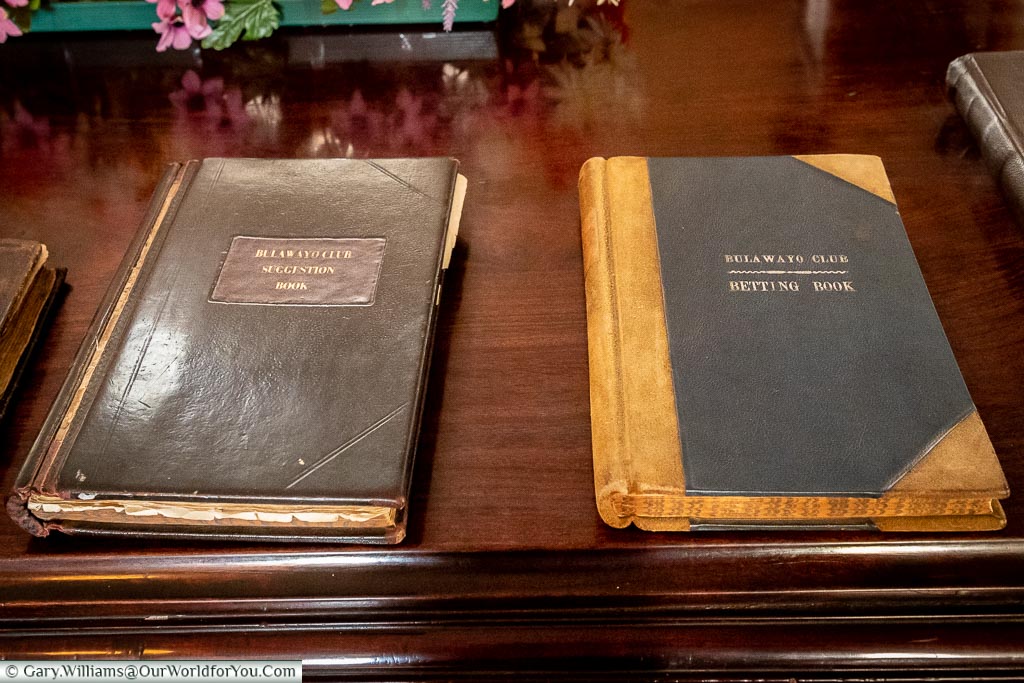 Two, rather old, leather bound, books on a wooden table. One is the Bulawayo Club Suggestion Book, the other os the Bulawayo Club Betting book.