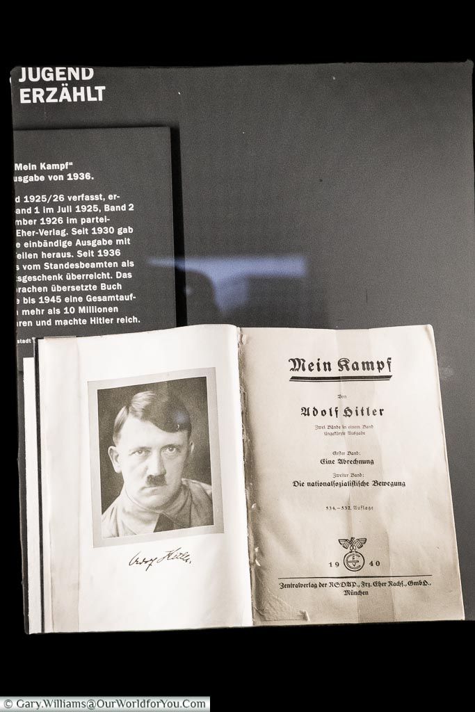 A museum exhibit of Mein Kampf open to the title page with a portrait of Adolf Hitler.