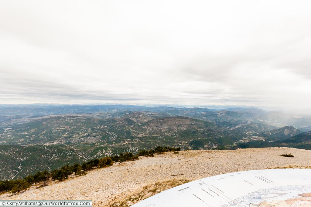 A view from the top of Mont Ventoux over the landscape to the north. A plaque points out the mountains in the range in front.