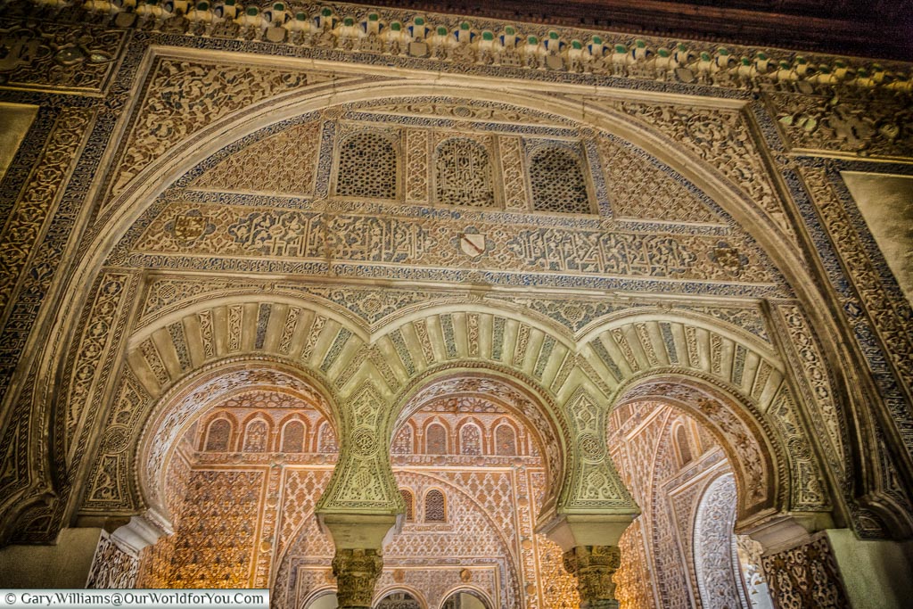A closeup look through one ornately decorated Moorish arch, to a room as equally ornate inside Seville's Alcazar.