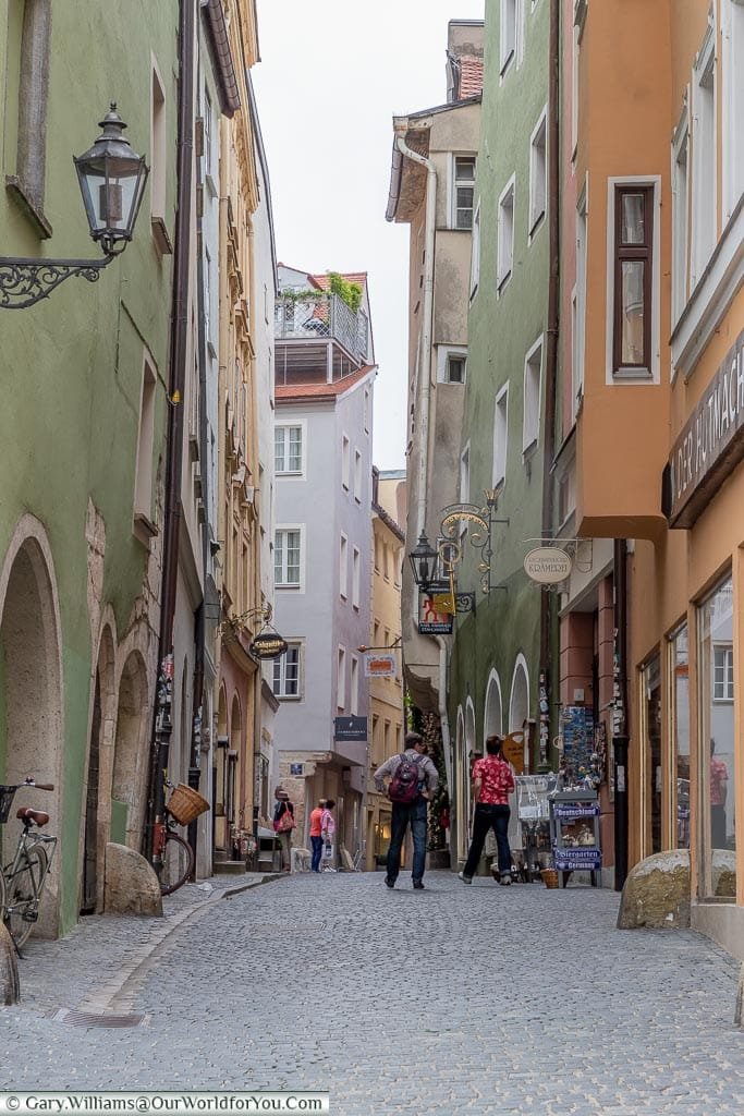 A narrow cobbled street view in the old town of Regensburg lined with shops.