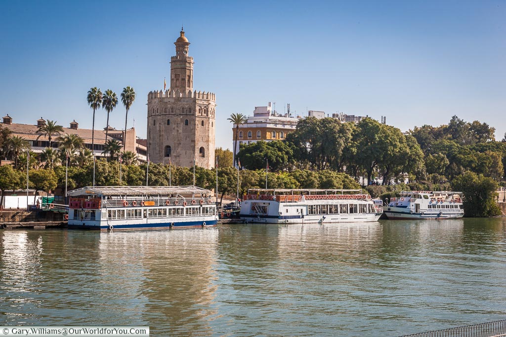 Tourist pleasure boats line the edges of the Guadalquivir river in front of the Moorish Torre del Oro.
