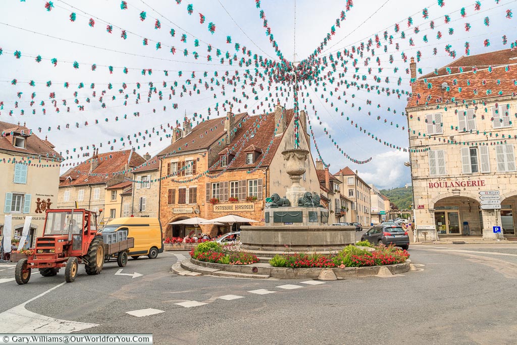 The fountain, acting as a roundabout in the centre of Arbois. Bunting leads from all corners of the square to meet at the fountain.