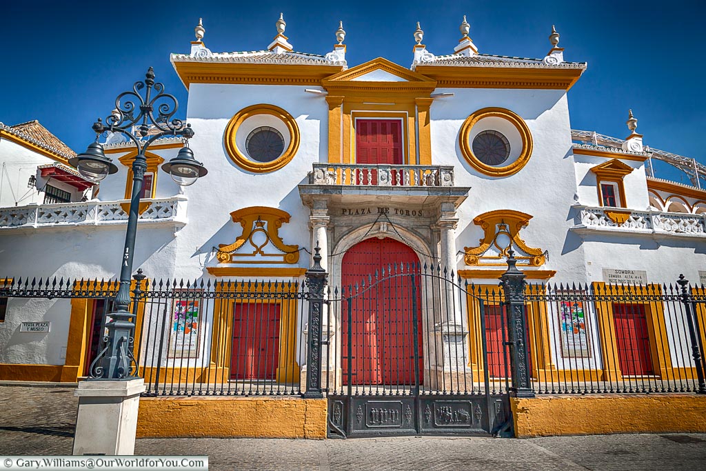 The traditional main entrance to Plaza de Toros, or bullring.  The doors are painted a deep red against a white building with Ocre coloured details.
