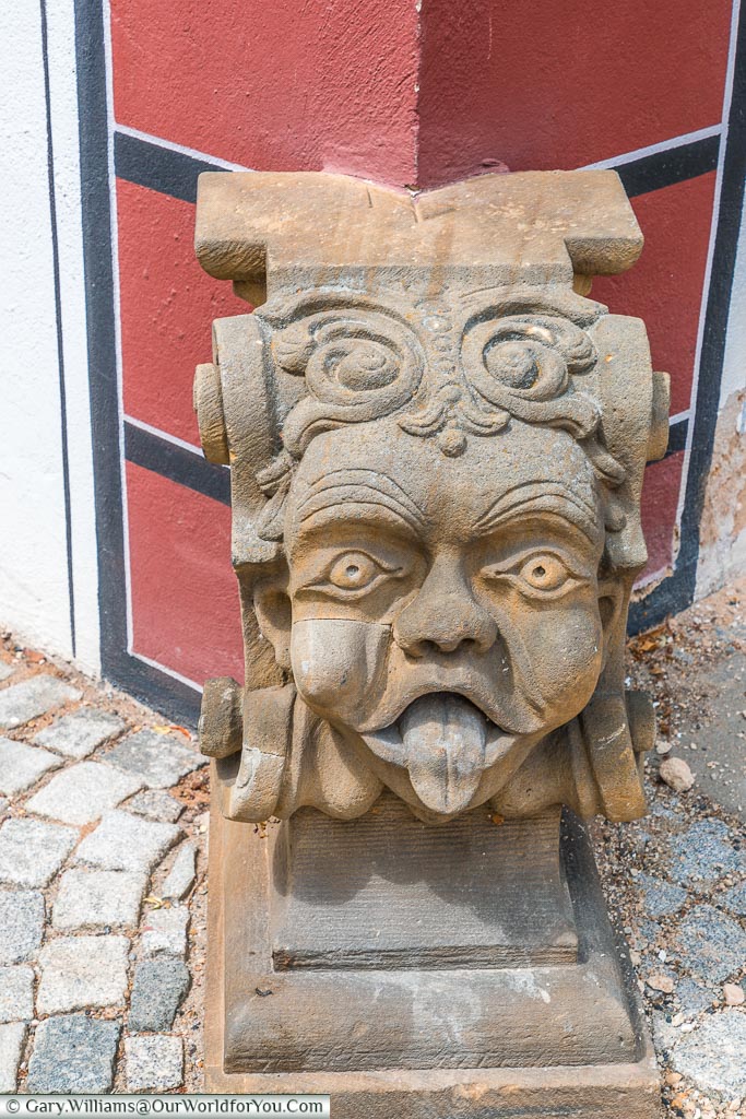 A stone decoration of a cheeky head with its tongue sticking out at the base of a house.
