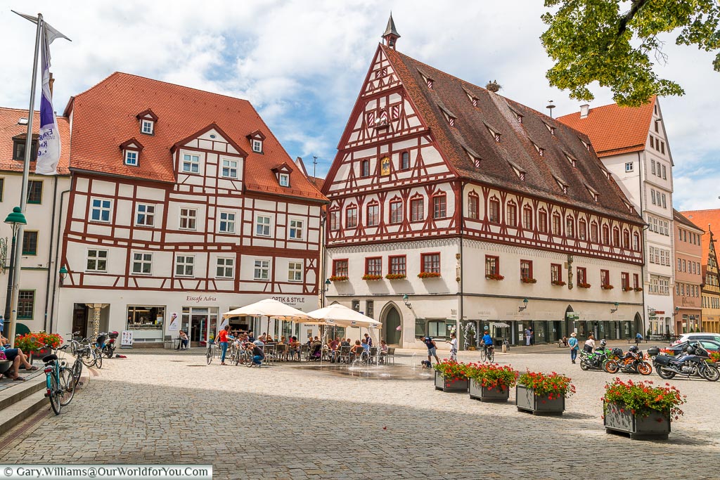 A view of the large, half-timbered, buildings that edge the pedestrianised Marktplatz with its sunken water feature, ice cream shop with tables & chairs outside.