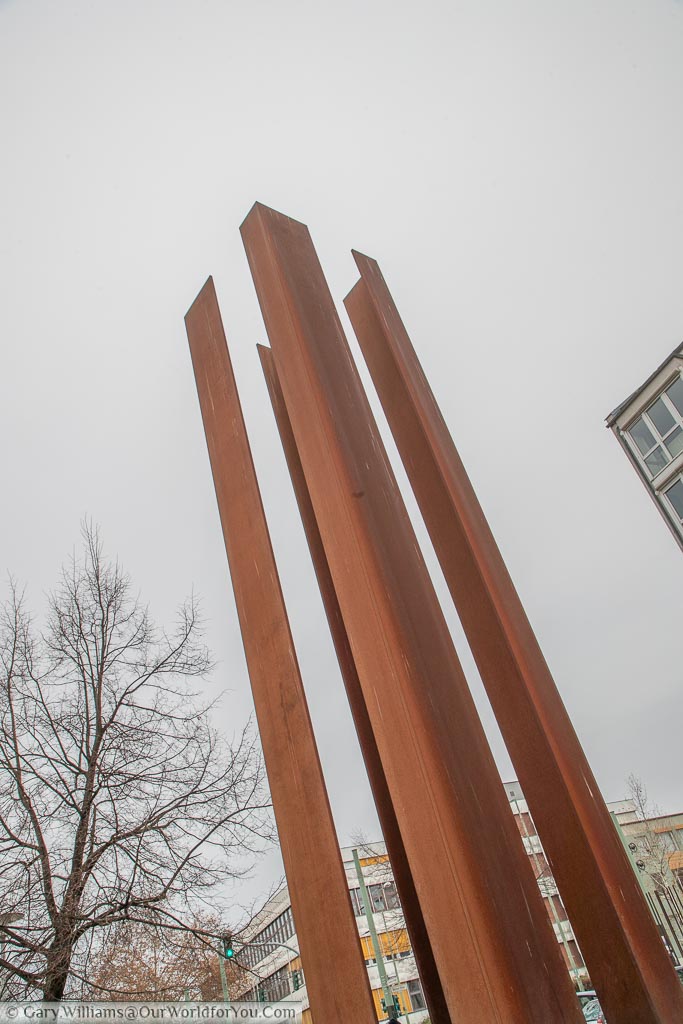 Four rusting iron girders pointing towards the sky representing of the Watchtower Memorial Strelitzer Strasse.