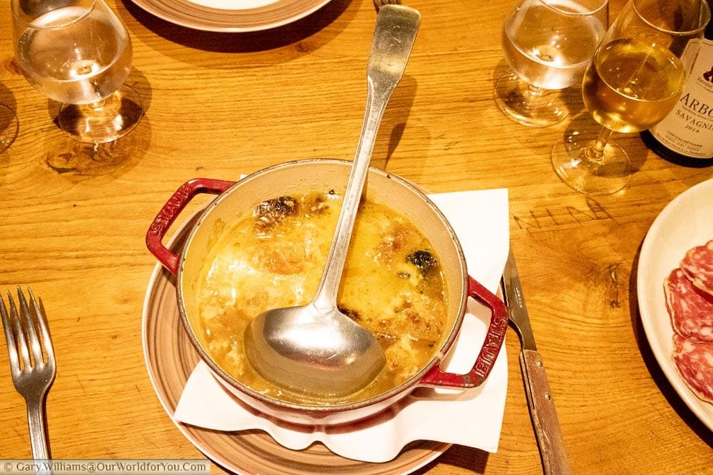 A large bowl of French Onion soup served in a cast iron cooking pot with a ladle to help yourself.