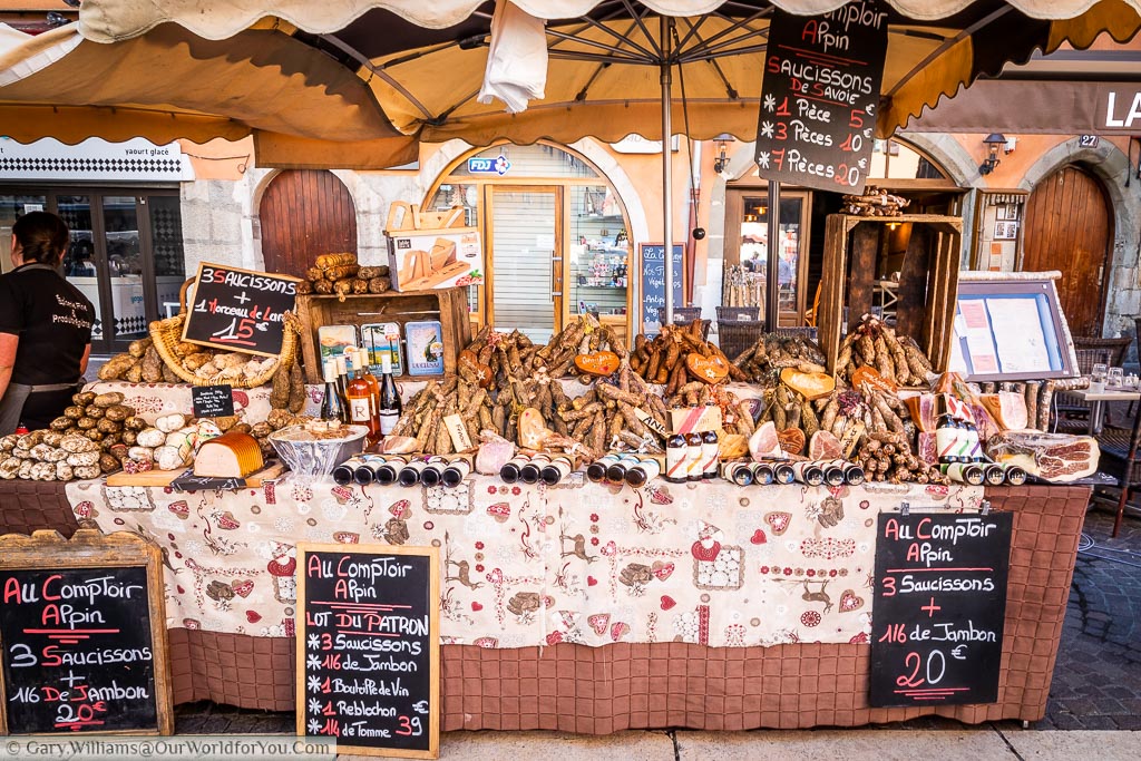 Stall in Annecy’s food market displaying regional cured hams, meats and  sausages.
