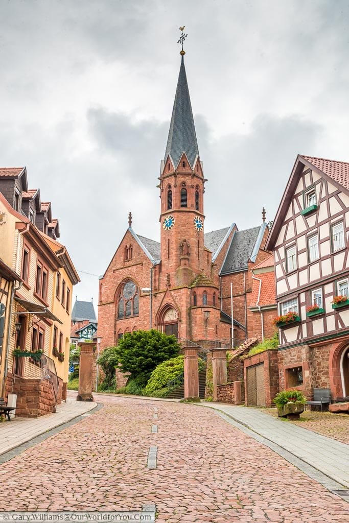 Looking up a cobbled street towards the red brick  Johannes church incorporating a narrow Bell tower.