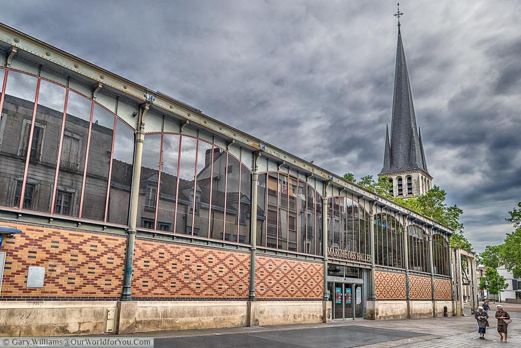 2 elderly women walking past the grand Marche des Halles in the city of Troyes on an overcast day.  The building Is home to an indoor market some supporting many local food traders.