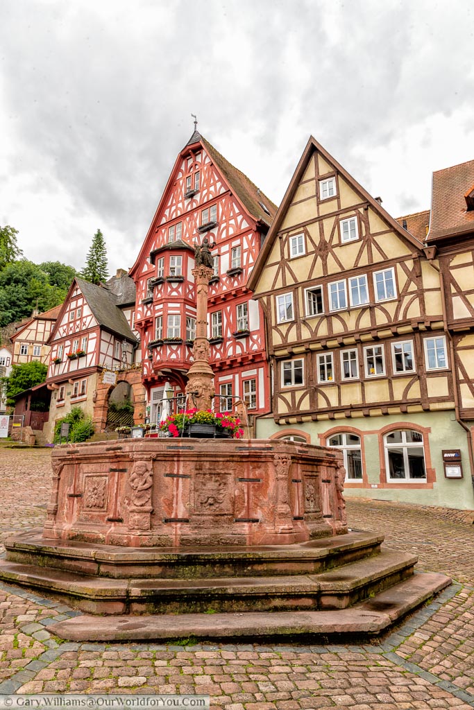 A red stone fountain, against the backdrop of the half-timbered houses of the Alter Marktplatz in Miltenberg