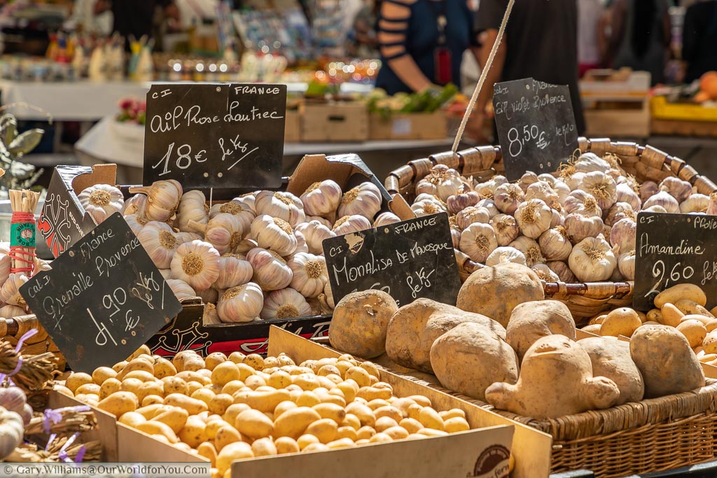 A stall in Nice, France, displaying varieties of potatoes and a selection of fresh garlic.