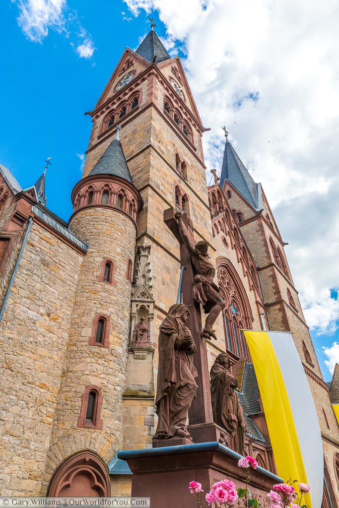 A portrait, wide angle view of a statue of Christ on the cross in front of the twin towers of the Cathedral of Bergstraße in Heppenheim.