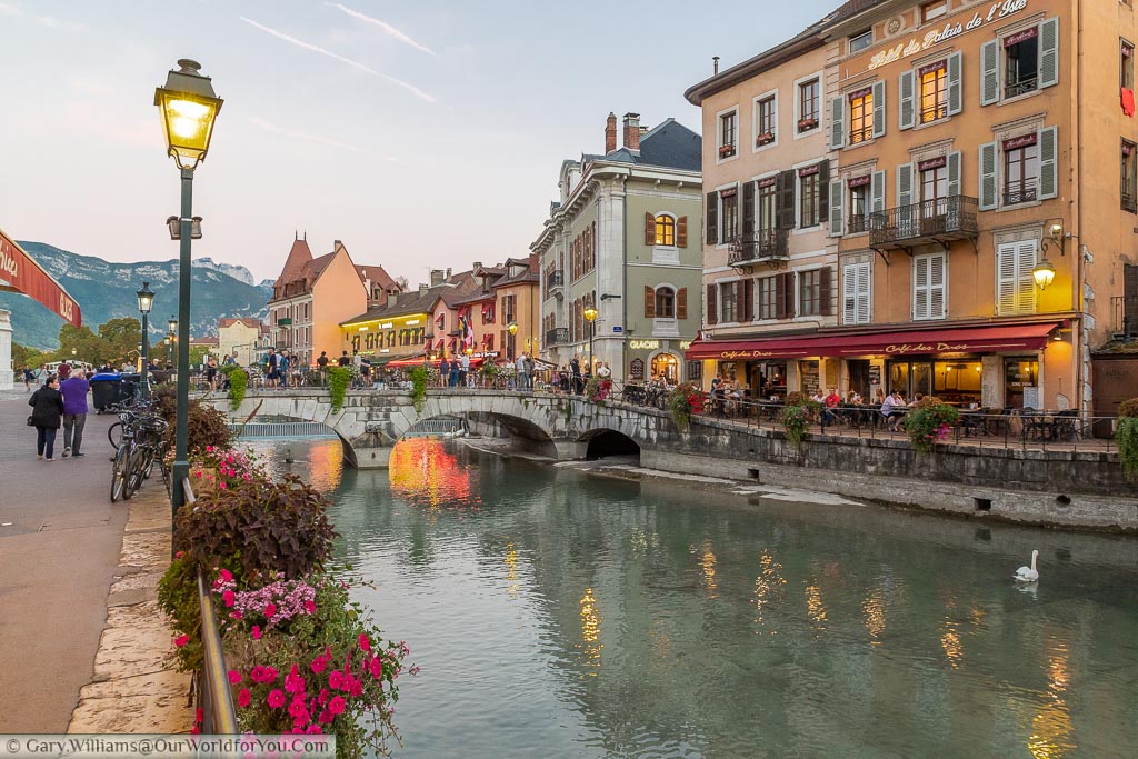 By the waters edge in Lake Annecy at dusk with restaurants lining the side of the canal