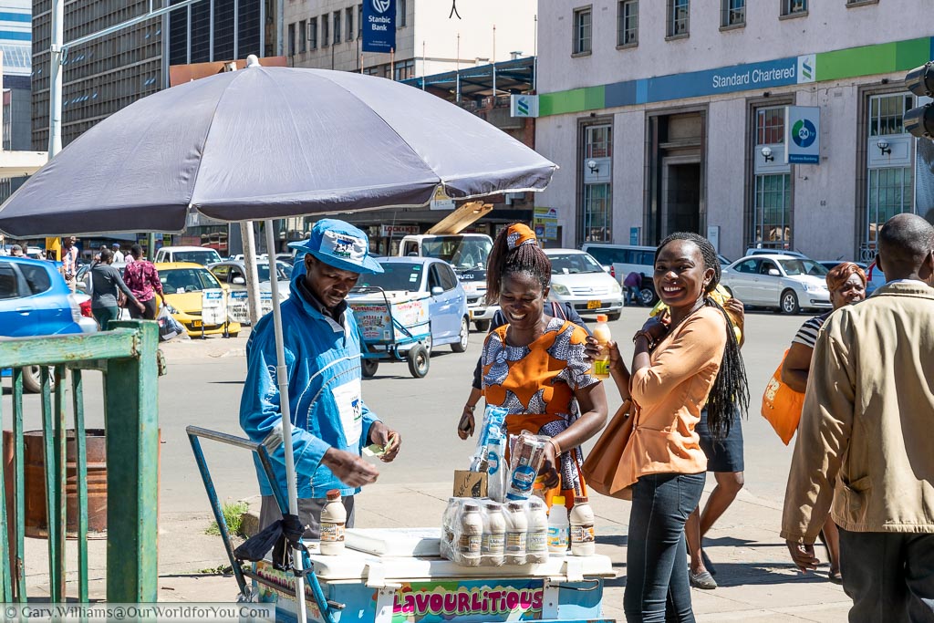 Two local women buying drinks from a street vendor in the centre of Harare.