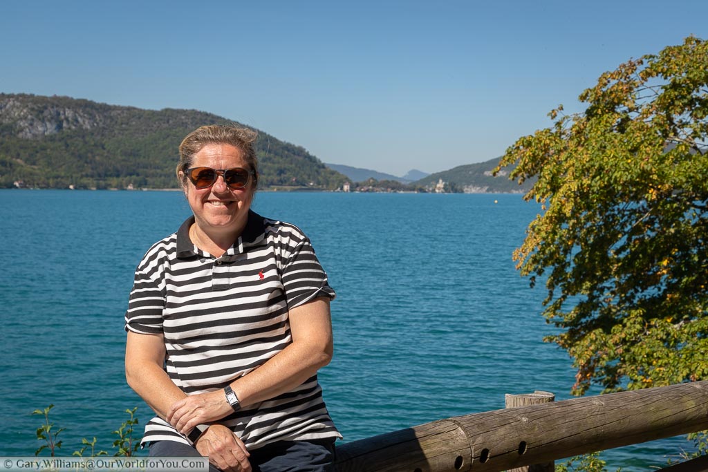 Janis sitting on a wooden fence in front of Lake Annecy in France