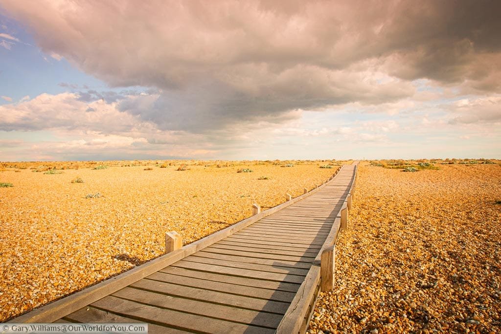 A wooden walkway leading across the pebbly beach of Dungeness Underneath a dramatic sky in the South East of England