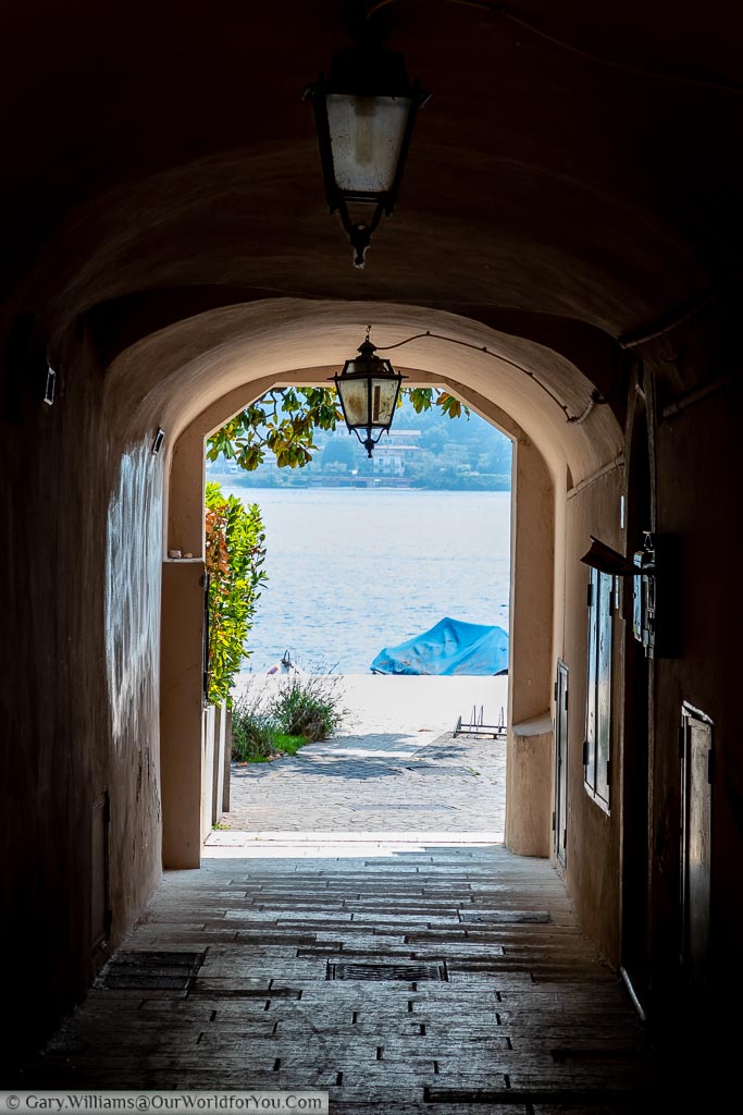 Looking through a darkened archway to a covered boat moored at the edge of Lake Garda