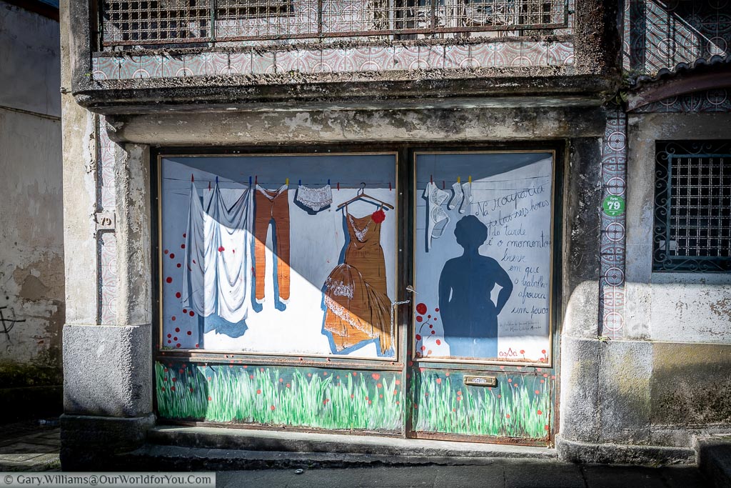 A mural on a shopfront in Amarante, Portugal, of a silhouetted woman next to a shopping line with clothes drying in the breeze.