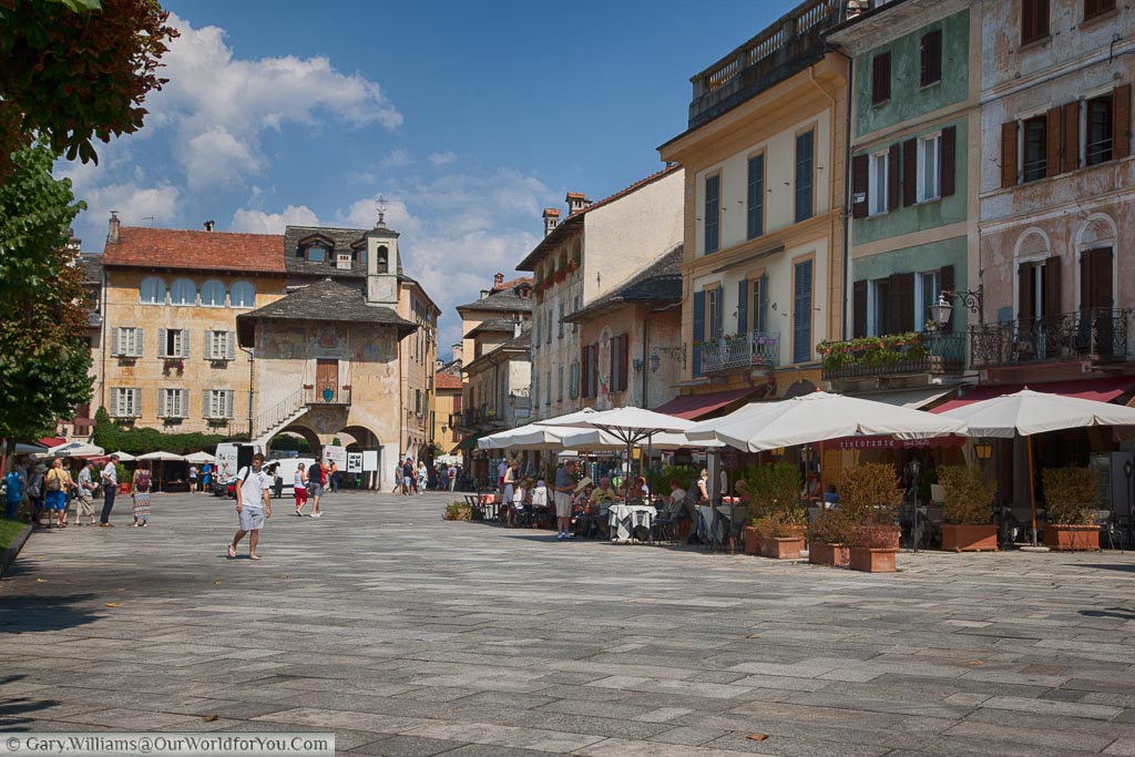 A historic square in Orta San Giulio, on the edge of Lake Orta,  lined with restaurants with al fresco dining areas our front with their parasols keep the sun off the dinners.