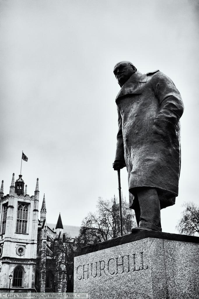 A black and white portrait shot of the Winston Churchill statue in Parliament Square, of him dressed in a heavy overcoat.