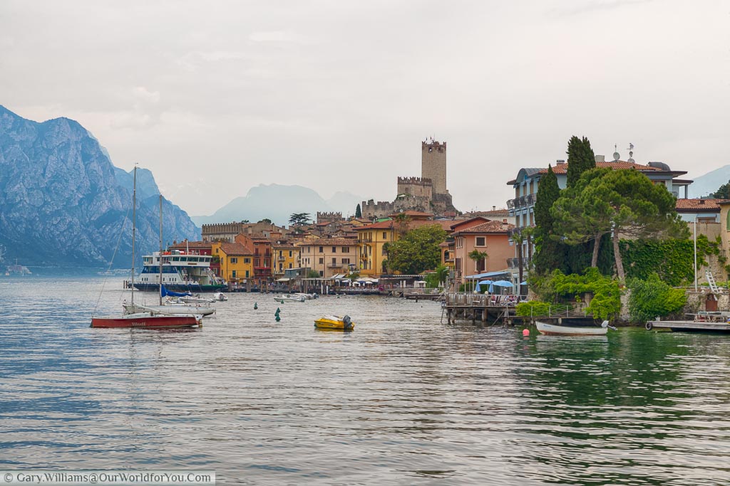 The pretty little lakeside town of Malcesine as seen from the water with boats bombing on the Lake and  with its Castle dominating the skyline.