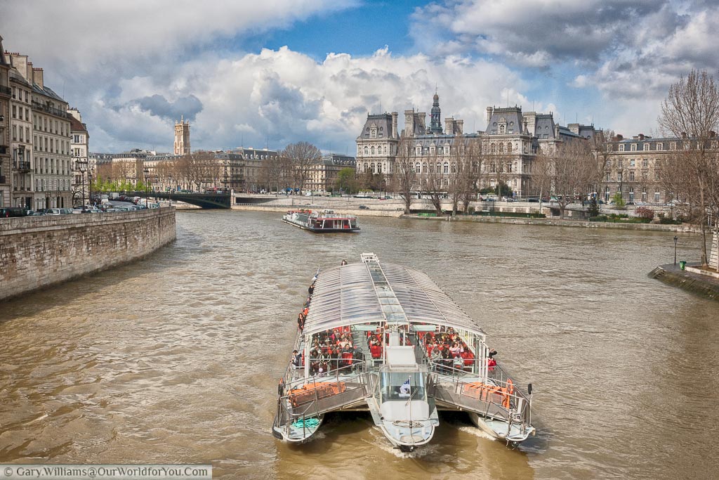 A pleasure boat on the Seine heading between the Île de la Cité and the Île Saint-Louis with the impressive architecture of Paris  as a backdrop.