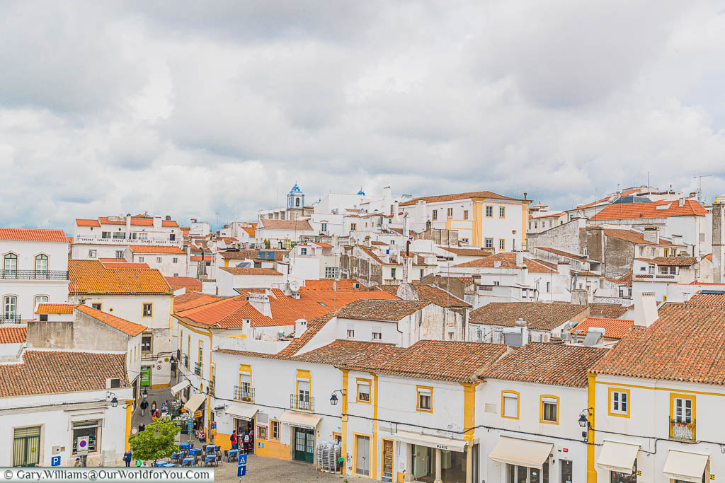 A rooftop view of the whitewashed building, trimmed in yellow, with their terracotta roofs, from the Igreja de São Francisco in Évora on a cloudy day.