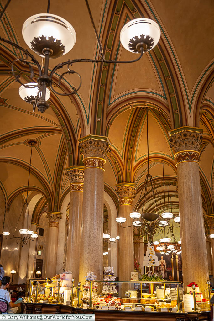 Inside the elegant Café Central in Vienna with it's high vaulted ceiling and decorative lighting.  In front of us is a pastry counter serving the elegant patisseries these cafés are renown for.