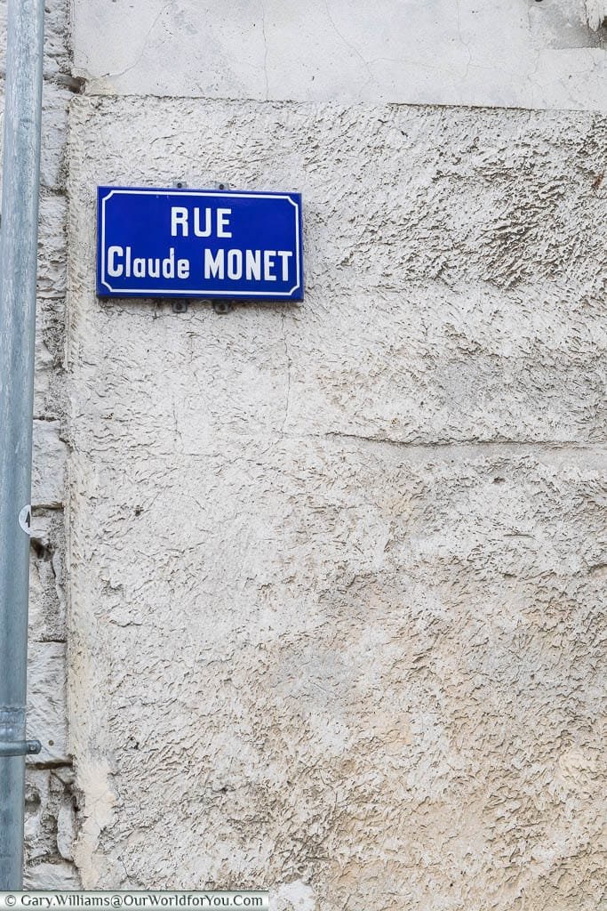 A traditional french street sign of white text on a blue enamel background for the Rue Claude Monet in Giverny