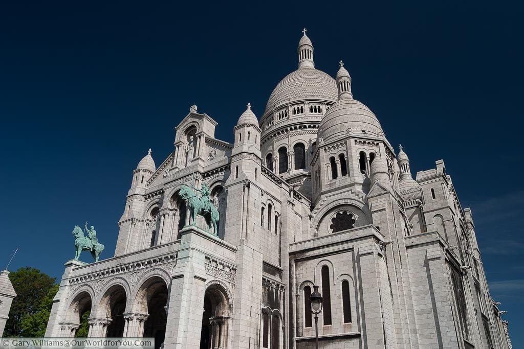 The white stone of the Sacré-Cœur Basilica in Paris set against a deep blue sky.