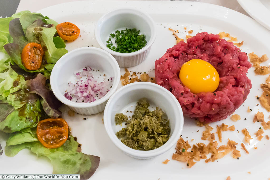 A plate of Steak Tartare prawns adorned with a raw egg yoke and all the rimming of chopped shives, capers & red onion in Cafe Magon in Caen, Normandy